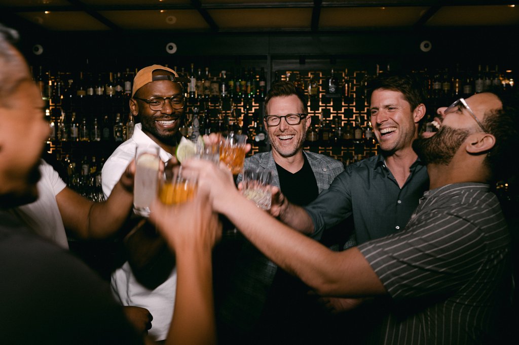 a group of five men laughing and toasting, holding glasses filled with alcohol at selva chicago the emily hotel