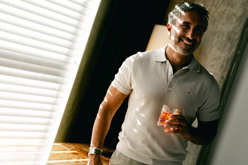 man in hotel room smiling with drink in his hand