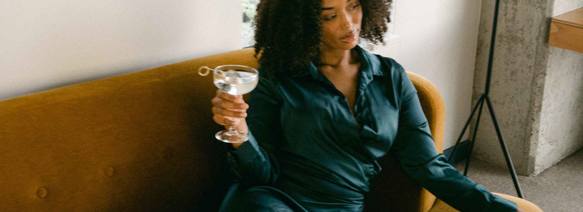 a girl in a blue dress sitting on the couch holding glass of martini in the loft suite at the emily hotel fulton market west loop