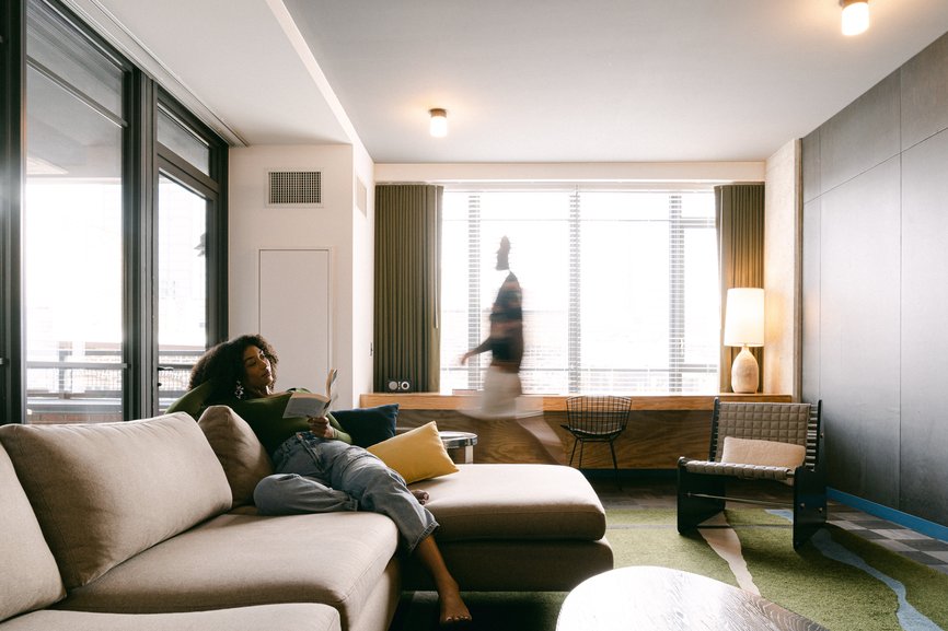 a girl reading a book in a large modern living room of the emily hotel suite with a man walking around in fulton market chicago