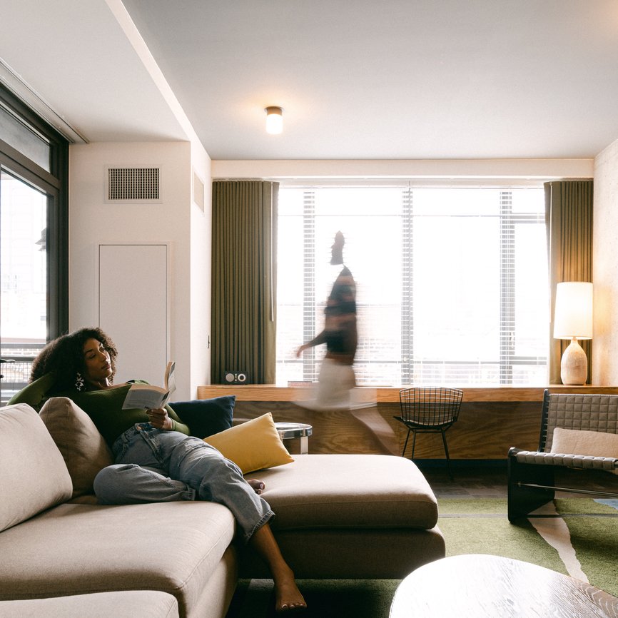 a girl reading a book in a large modern living room of the emily hotel suite with a man walking around in fulton market chicago