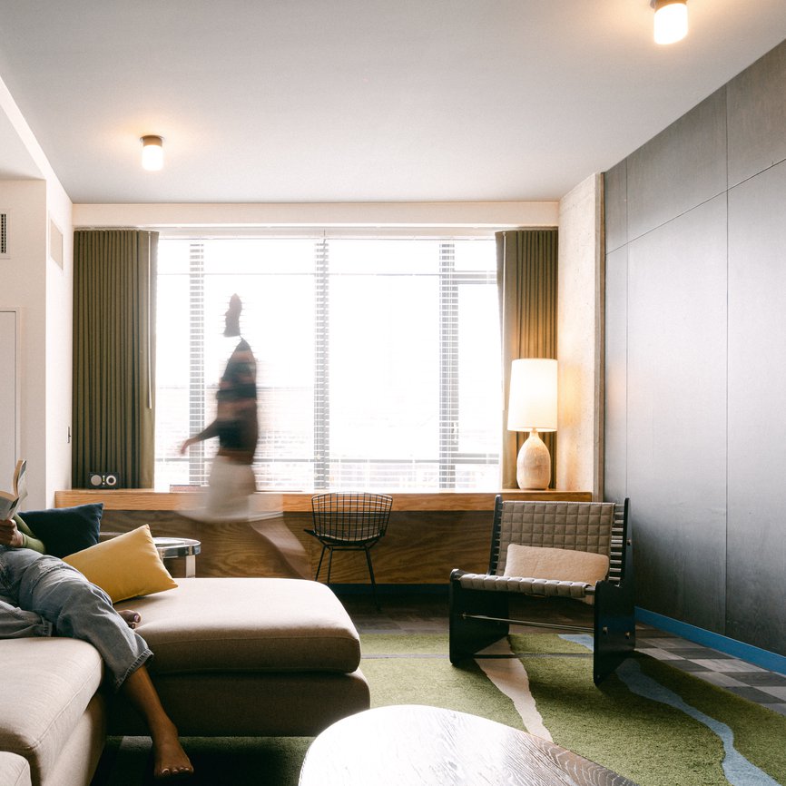 a girl reading a book in a large modern living room of the emily hotel suite with a man walking around in fulton market chicago