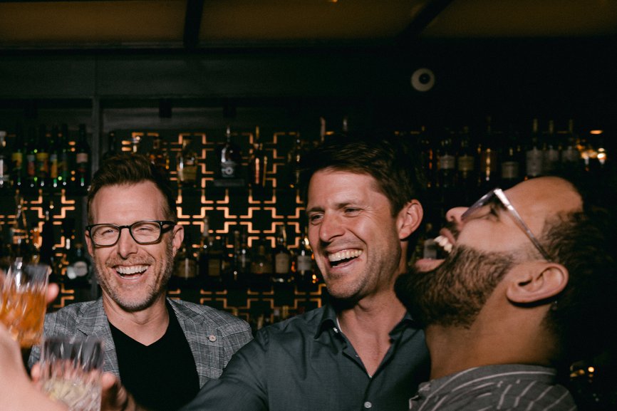 a group of five men laughing and toasting, holding glasses filled with alcohol at selva chicago the emily hotel