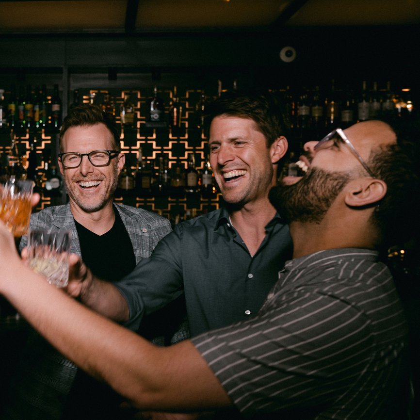 a group of five men laughing and toasting, holding glasses filled with alcohol at selva chicago the emily hotel