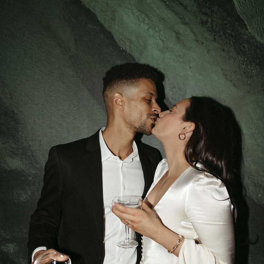 a newly wedded couple kissing each other with a glass of white wine on hand posing for a photo at the emily hotel