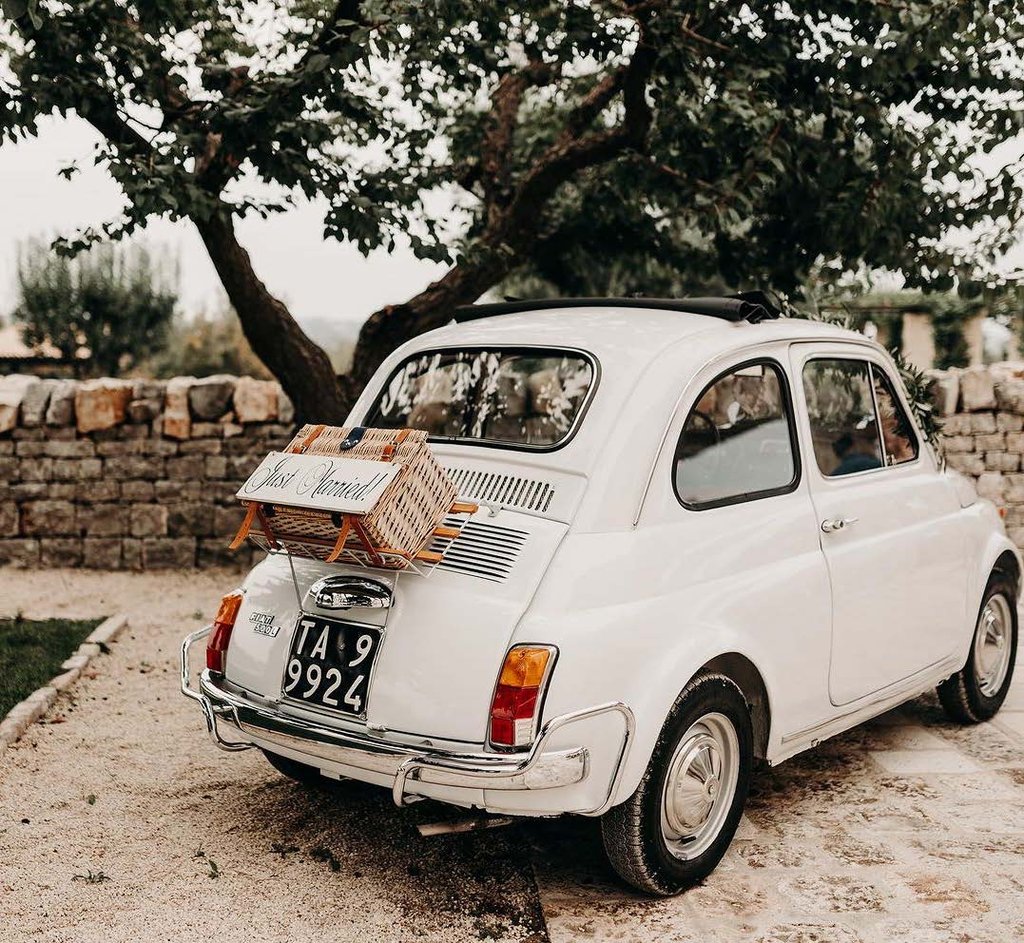 a white vintage fiat 500 with a wicker basket on the back with a sign that says just married at villa torre bianca by emily hotels puglia