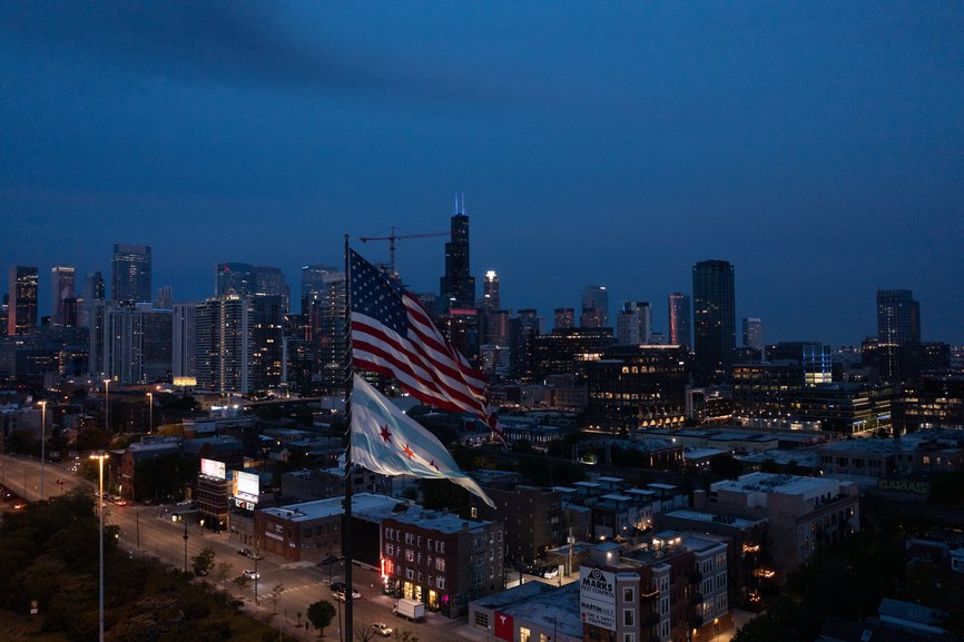 nighttime view of the city skyline of chicago with two american flag and chicago city flag