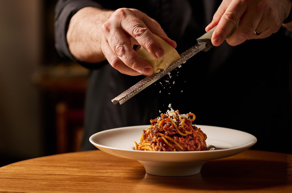 Chef marcello garnishing chittara ragu with cheese