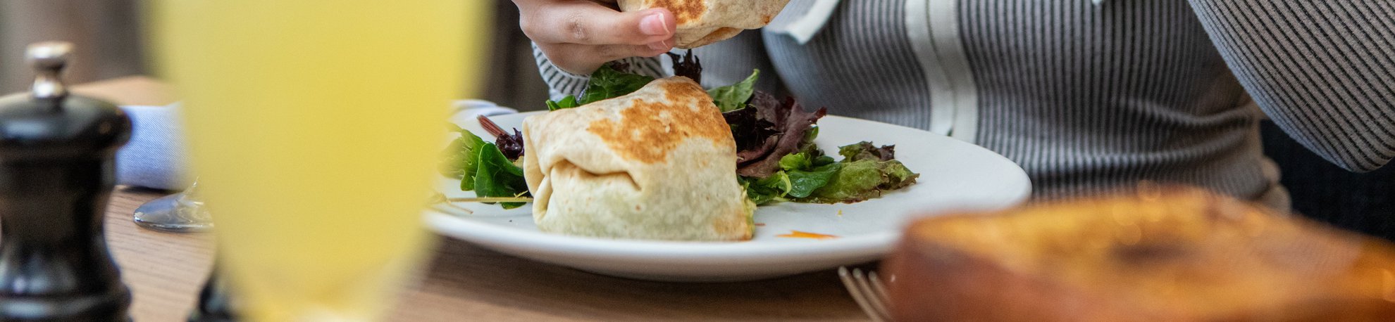 woman pouring sauce on breakfast burrito smiling , blurred mimosa in front